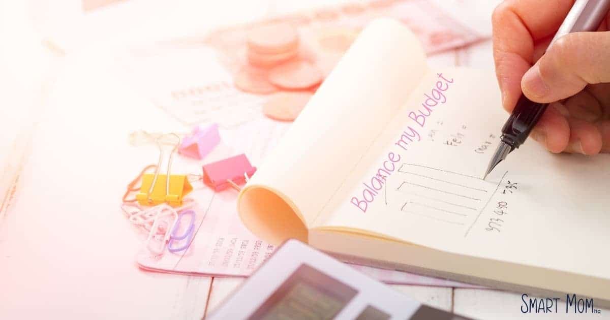 clipboard on table with pastel background colors writing says balance your budget