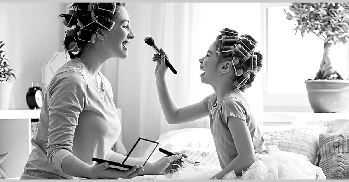 home life category page mom and daughter with rollers in hair putting on makeup sitting on bed